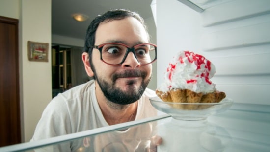 איש מצחיק מסתכל על עוגה במקרר, מצב מוכר של אכילה רגשית